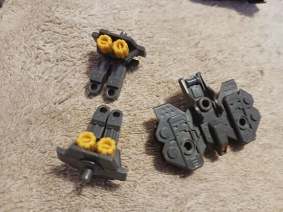 A photograph of the wild weasel base, disassembled. They actual weaponry is already repurposed and will find its final home soon, but the base itself consists of a platform and two "arms" which provide a 3mm peg to mount things directly off of. The first attempt at this customization involved a 5mm-to-3mm hole adapter and using the arms, but the weight strain was pretty bad there as well.

Still, on the final version of this I'll probably want to go that route. I'm not sure how to get another adapter like that without buying an entire extra set of booster cannons, not exactly ideal.