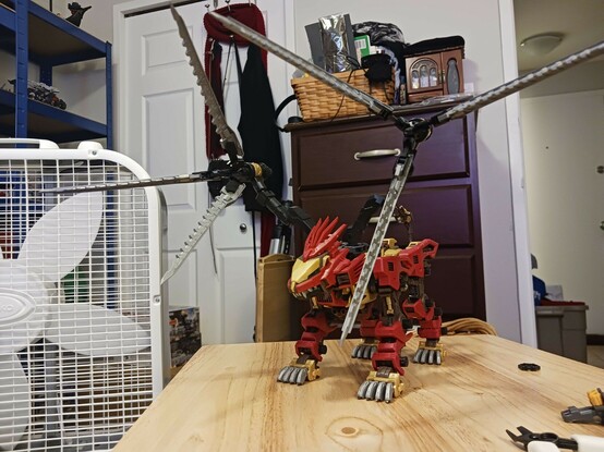 A photograph of Edgar, its new weaponry deployed. Edgar itself is a red lion Zoid with gold accents and a brown body under the armour, and the deployed buster claws give it a massive  height and width profile. They open up to create a triangular arrangement of silver claws converging on a central point consisting of a gun barrel. The arms connecting them are a little awkward, but fold nicely and can be arranged to give them a decent amount of clearance from each other.