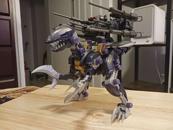 Another photograph of Sirius, now armed with a backpack made mostly of Abigail's old wild weasel parts, arranged to fit the profile of a rev raptor's frame better. It consists of a middle frame (taken from the booster cannons built a few weeks ago in this case) with a largeish gatling gun to each side, and a pair of long rifles attached to the sides of those. On top of each gatling gun is also a three-warhead missile launcher, the tips coloured red by eyeliner of course. Sirius is striking a much more threatening, widely-spaced pose partly to balance the added weight of the backpack forward a little bit. The blades still have a little room, and the way they extend out would allow them to be used, albeit a bit awkwardly compared to a normal raptor.