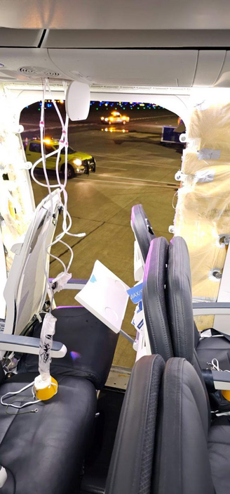 A photo of a seat in an Alaska Airlines 737 Max showing all the black padding ripped off, there's a huge but neat hole in the plane showing a car outside parked on the tarmac. The oxygen masks are deployed. 