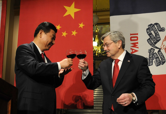 Chinese President Xi Jinping and Iowa Gov. Terry Branstad raise their glasses in a toast at a State Dinner at the state Capitol in February 15, 2012. They are both holding the red wine glasses by the stem and Xi has a Chinese flag behind him, and Branstad has an Iowa state flag behind him. 
