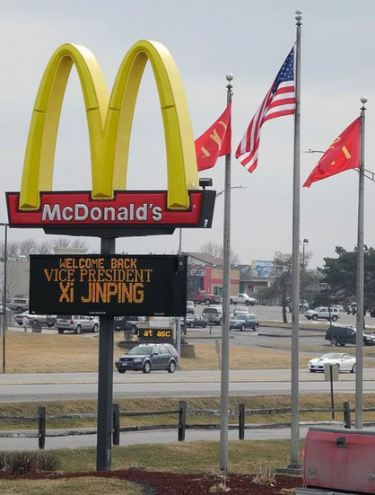 A photo of the McDonalds in Muscatine, Iowa, showing a sign reading "Welcome Back Vice President Xi Jinping" with 2 McDonalds flags and an American flag in the background.