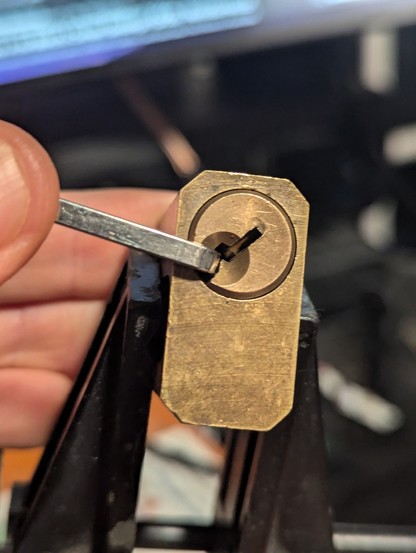 A brass 5 pin practice lock sits in a panavice jr. The lock is at 45 degrees show that it's unlocked. This practice lock can take different lock mechanisms but I only have the one. Im also not sure how to replace the mechanism as I stole this and the tools from an asshole.🤣