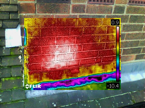 A thermal camera image of a brick wall showing a hot spot on the lower left hand corner and a general radiating warm from it. 