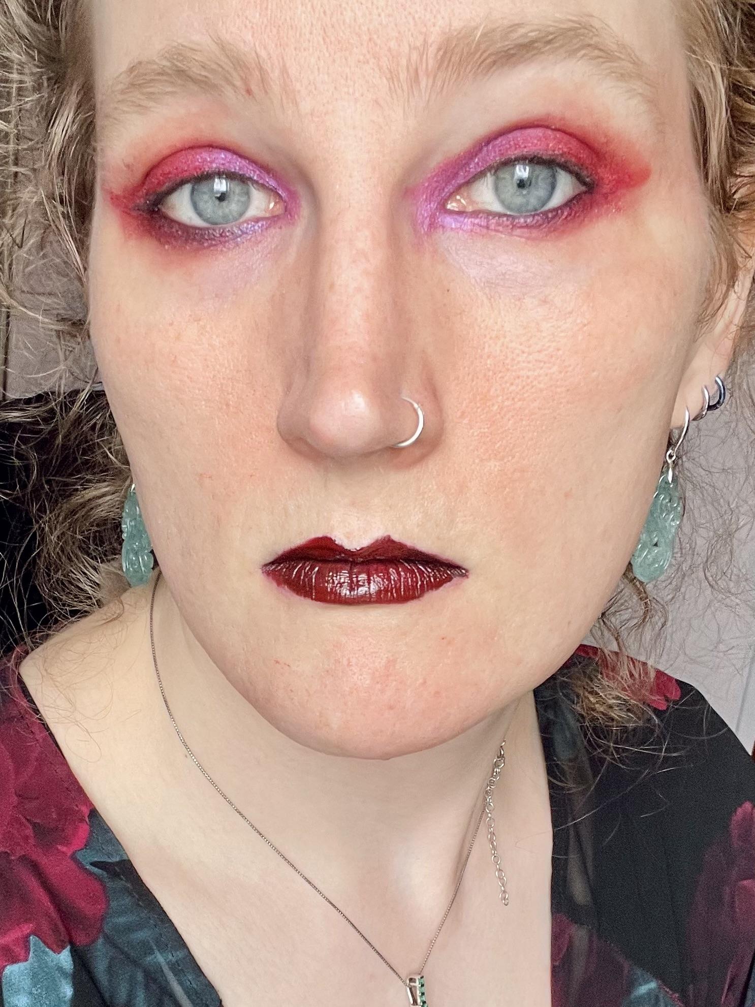 Selfie of a white woman with vibrant red and pink eyeshadow and dark red lipstick