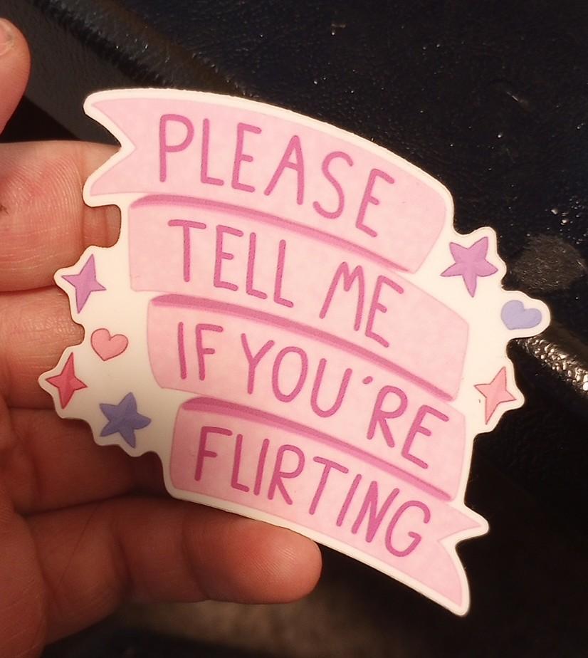 on a sticker, a pink ribbon with the words "please tell me if you're flirting".